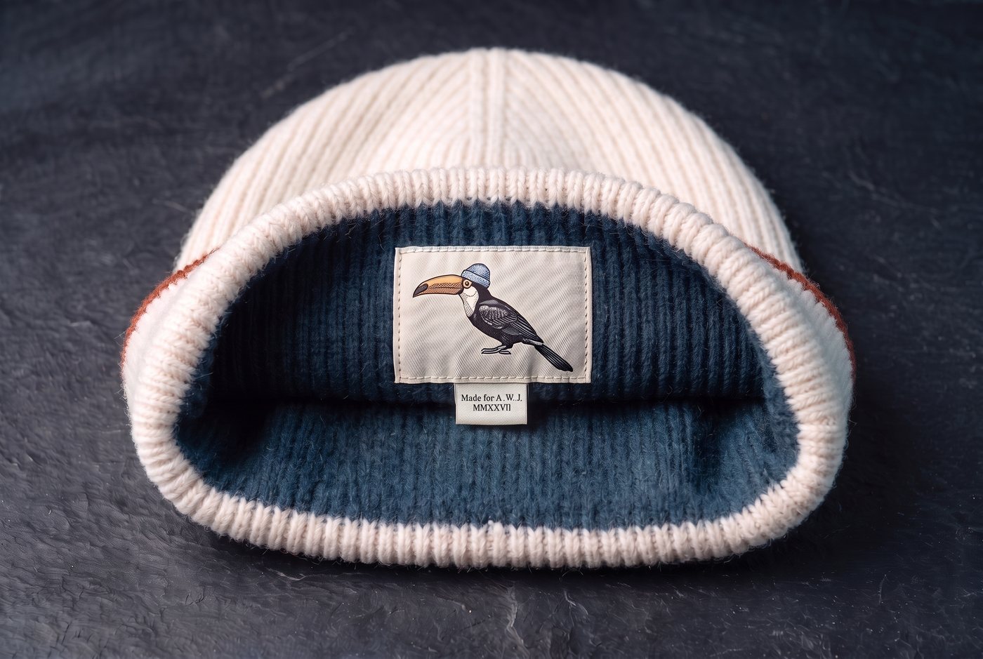Looking down into a chalk Rare Bird: the inside of the cuff lined in brushed petrol cashmere, the small woven label with the toucan sewn on the lining, its tag reading Made for A. W. J., MMXXVII.